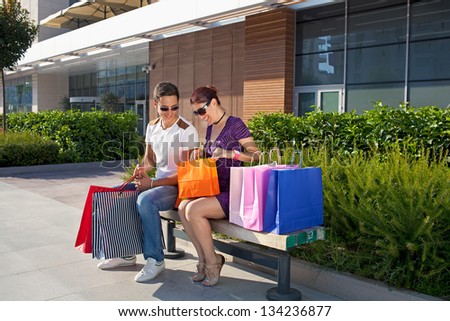 Happy young couple shopping. Happy young couple sitting on a bench in front of a shopping mall with colorful shopping bags, relaxing