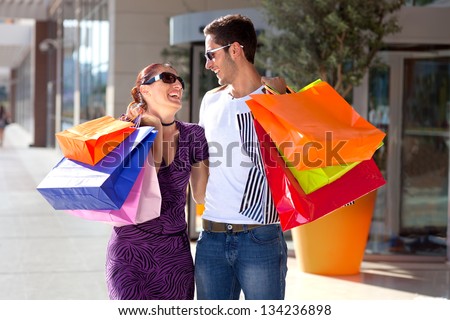 Young couple enjoying shopping. Happy young couple embracing each other, having fun during shopping, carrying colorful shopping bags