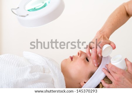 Beautician applying cream on the face of a woman. Beautician applying facial cream on the forehead of a relaxed blond woman