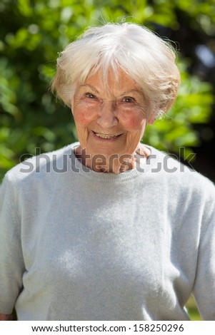 Portrait of a smiling senior woman. Head and shoulders portrait of a grey haired smiling senior woman or grandmother standing in sunshine in the garden