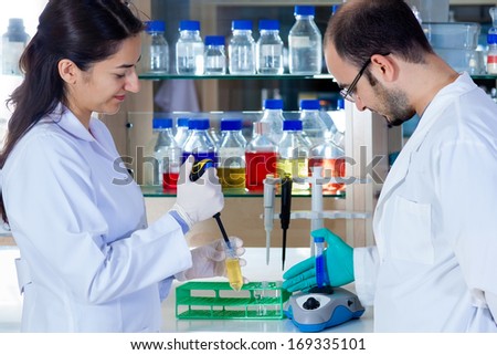 Male laboratory technician at work mixing a solution in a test tube on a centrifuge with a female colleague waiting to add more sample with a pipette