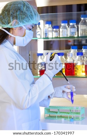Female lab technician at work in a laboratory standing with a test tube in her hand, transferring a measured amount of the chemical solution or sample using an automated pipette.