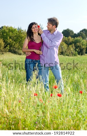 Loving young couple in a poppy field laughing and smiling as the young man puts a red poppy flower in his girlfriends hair as they stand in the summer sunshine