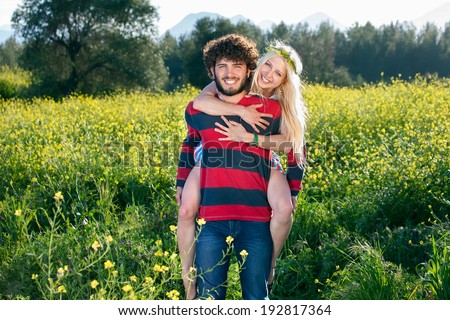 Playful young couple in a yellow rapeseed field smiling happily at the camera as the young man gives his beautiful young girlfriend a piggy back ride