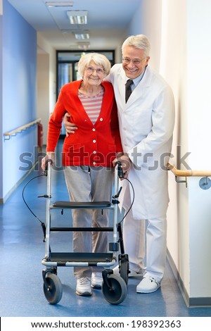 Physician helping a senior woman in a walker supporting her with an arms around her shoulders as he assists her with the walking frame