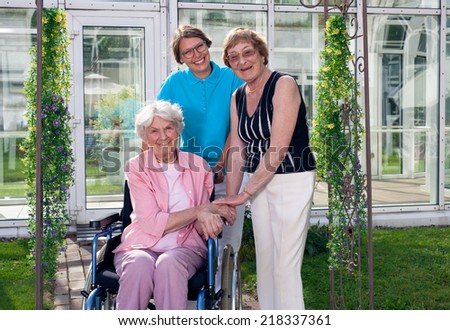 Happy Caregiver for two Elderly Patients at Home Garden Looking at Camera. Captured with Glass Building at the Background.