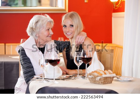 Old and Young Blond Women at Table Having Snacks at the Restaurant with Wine, Water and Bread on the Table.