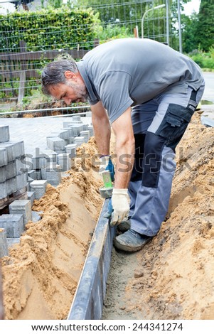 Worker separate a private property from public street by putting narrow stone slabs vertical into the ground.