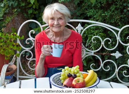 Close up Smiling Old Woman Having a Cup of Coffee at the Garden Table with Fresh Fruits.