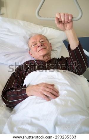 Frail senior man lying in a hospital bed on a ward recuperating from an illness or operation lying resting with his glasses on and eyes closed and a quiet smile
