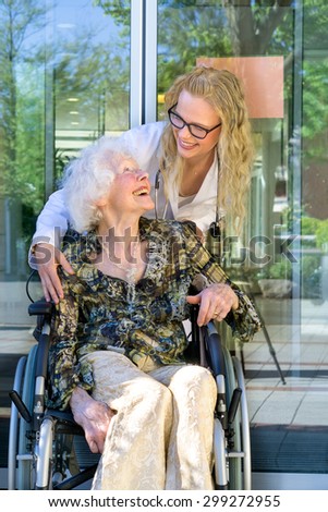 Young Medical Assistant and her Elderly Woman Patient on a Wheelchair Laughing Together Outside the Nursing Home.