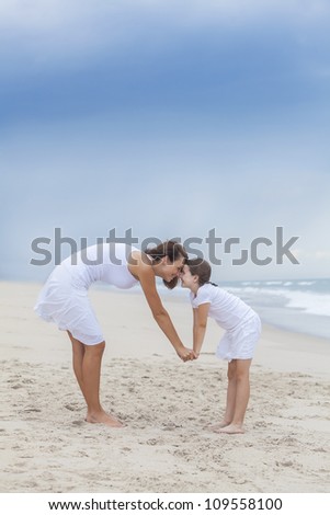 A happy woman and girl, mother & daughter having fun rubbing noses on a sunny tropical beach