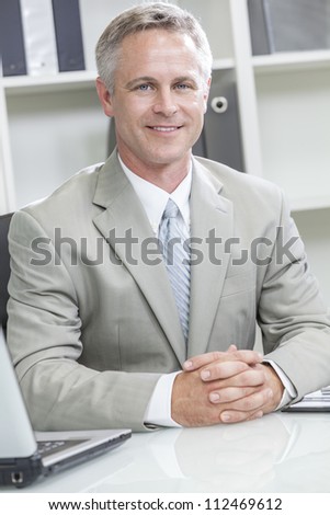 Happy smiling man or businessman sitting at desk in modern office