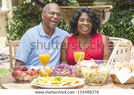 A happy, smiling man and woman senior African American couple eating healthy food at a picnic table outside
