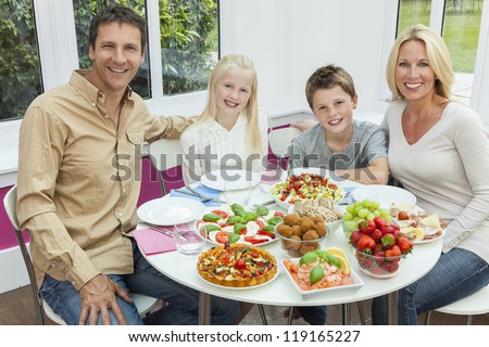 An attractive happy, smiling family of mother, father, son and daughter eating healthy salad at a dining table.