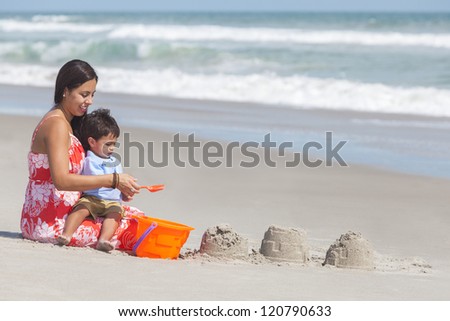 A happy hispanic mother and young child boy son having fun in the sand together making sand castles on a sunny beach