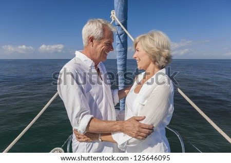 A happy senior couple embracing at the front or bow of a sail boat on a calm blue sea looking to a clear horizon