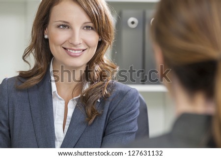 Beautiful young woman or businesswoman in smart business suit sitting at a desk in an office having a meeting