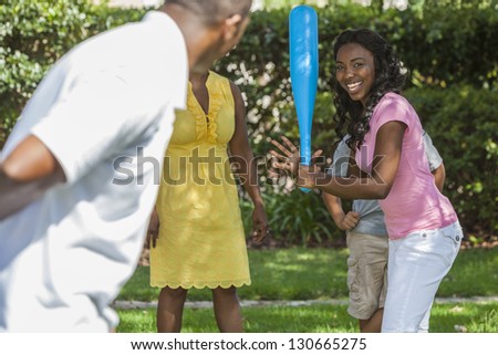 African American family, man, woman, girl and boy children, mother, father, son & daughter playing baseball together outside.