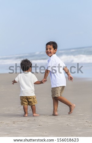 Two happy young hispanic boy children brothers playing together on a beach