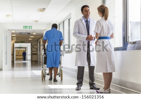 Asian male doctor & female nurse in hospital corridor with African American black nurse & senior female patient in wheelchair
