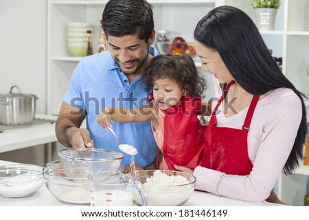 Asian Chinese family, man & woman parents and young girl child daughter cooking, baking, making cakes in home kitchen