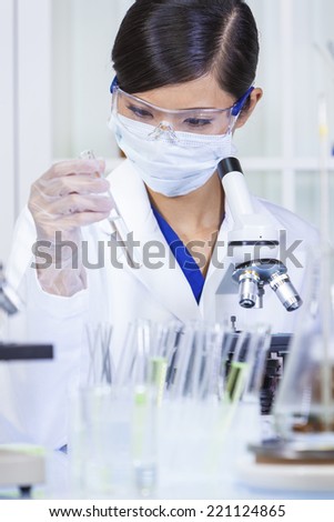A Chinese Asian female medical or scientific researcher or doctor with test tube & using a microscope in a laboratory