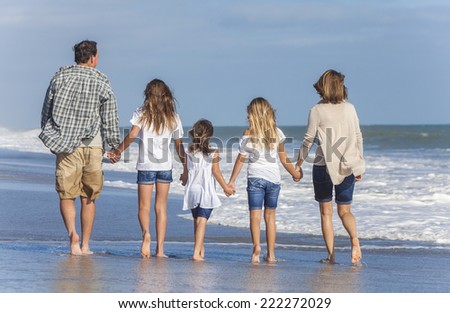 Rear view of family mother, father, daughter, parents and female girl children walking in the sea on a beach