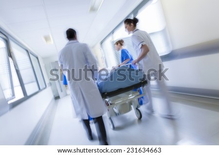 A motion blurred photograph of a patient on stretcher or gurney being pushed at speed through a hospital corridor by doctors & nurses to an emergency room Stock fotó © 