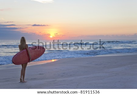 Rear view of three a young women surfer girl in bikinis with red surfboard on beach at sunset or sunrise