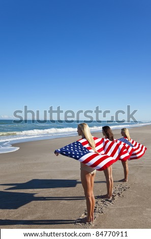 Three beautiful young women wearing bikinis and wrapped in American flags on a sunny beach