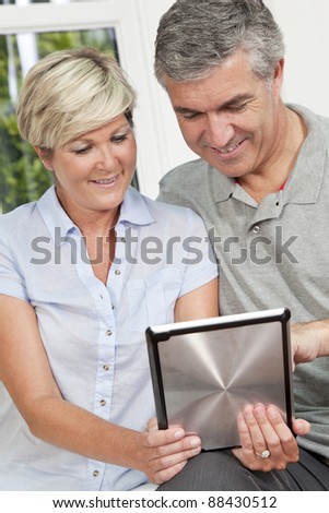 Portrait shot of an attractive, successful and happy middle aged man and woman couple in their forties, sitting together at home on a sofa using tablet computer