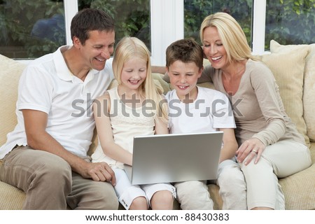 An attractive happy, family of mother, father, son and daughter sitting on a sofa at home having fun using a laptop or computer