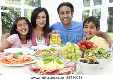 An attractive happy, smiling Asian Indian family of mother, father, son and daughter eating healthy food & salad at a dining table.