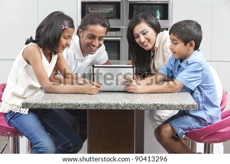 Asian Indian family husband & wife, children, girl and boy, using tablet computer in the kitchen at home