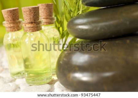Spa massage hot stones and small bottles of liquid or essential oils in natural green environment