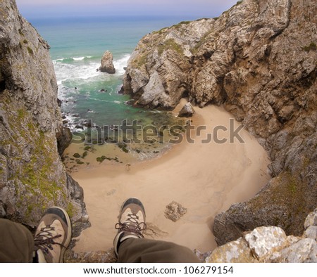 Feet hanging from a cliff over a small, inaccessible, deserted beach. Sintra, Portugal.
