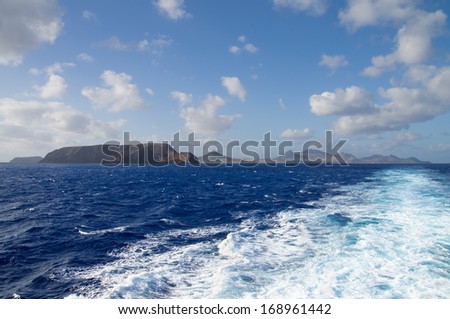 Porto Santo Island as seen from the cruise ship that leaves it. Ship wake under blue sky and over blue sky. Madeira, Portugal.