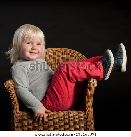 Little girl laying in a cane chair isolated on a black background