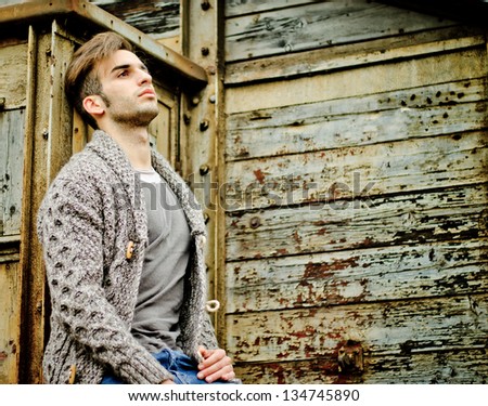 Good looking guy leaning against rusty metal and wooden walls