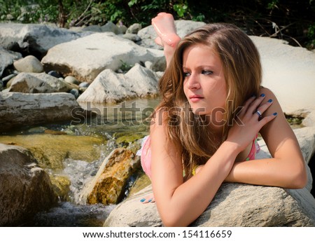 Pretty brunette girl in bikini laying on rocks by small water stream