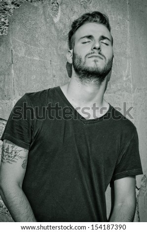 Attractive young man with black t-shirt, against rough wall, with eyes closed