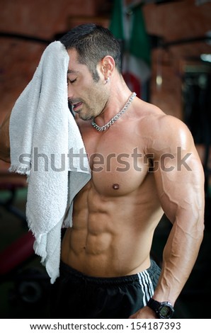Muscular bodybuilder drying sweat from his face with a towel after workout in a gym