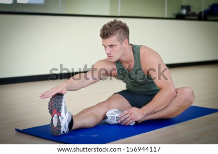 Attractive young man stretching on gym mat, touching foot with hand