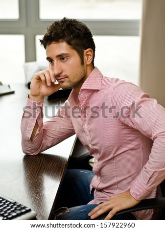 Attractive young businessman sitting at desk in his office in front of computer