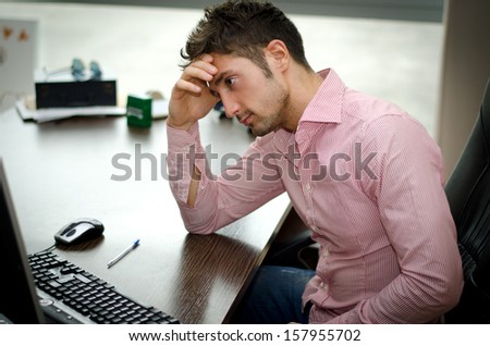 Preoccupied, worried young male worker staring at computer screen in his office