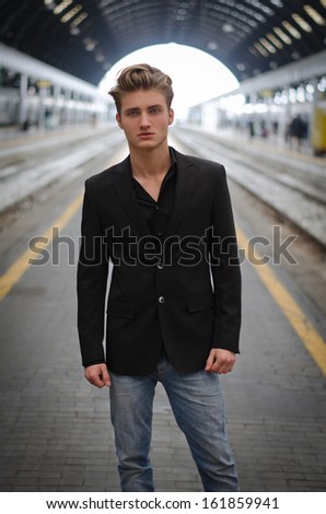 Handsome blond young man standing inside a train station, looking in camera