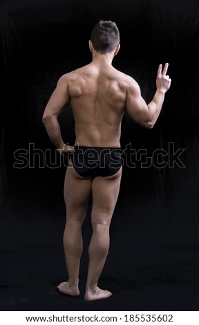 Back of muscular young man doing peace sign. Full length body shot on black
