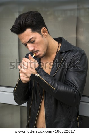 Handsome young man with leather jacket on naked torso lighting up a cigarette