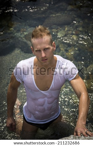 Attractive young bodybuilder by the sea with wet t-shirt on, serious expression